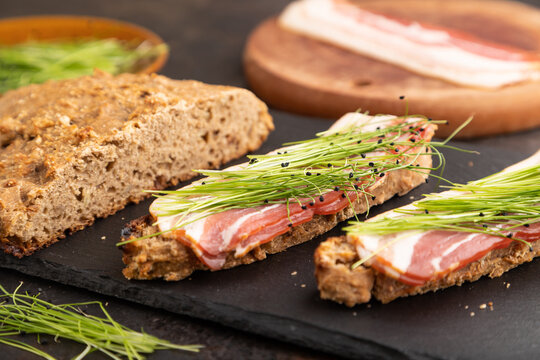 Bread sandwiches with jerky meat and lard with onion microgreen on black concrete. side view, selective focus.