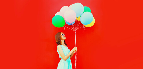 Happy young woman with bunch of colorful balloons on red background