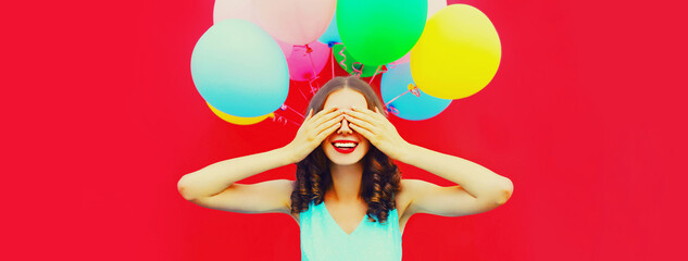 Portrait of happy surprised woman making wish covering her eyes with hands on colorful balloons on...