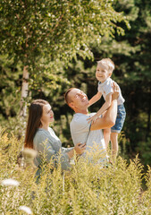 Happy young family of three spend time together and smiling while standing in nature.