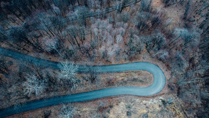 Aerial high angle view of narrow winding curvy mountain road among the trees in winter forest. Bird's eye view landscape.