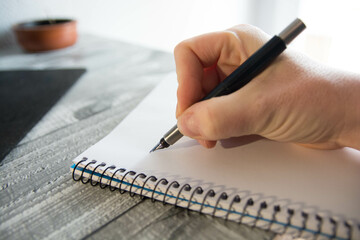 Mano sosteniendo pluma de escritura sobre libreta