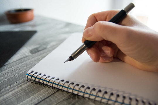 Mano sosteniendo pluma de escritura sobre libreta