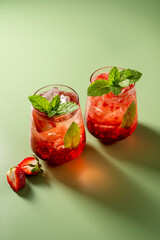 Refreshing strawberry summer drink glasses with ice cubes and mint leaves. Green background.