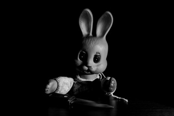 A toy rubber bunny sits with a knife at the table. Creepy rabbit with glowing eyes