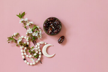 Ramadan food and drinks concept. Ramadan Islamic rosary beads, white flowers and dates fruit on a light pink background. Iftar dinner. Top view flat lay. Copy space.