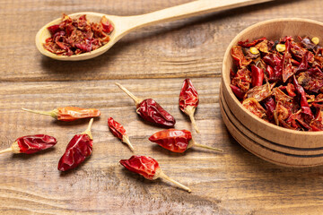 Pods of dry red pepper in wooden bowl and on table.