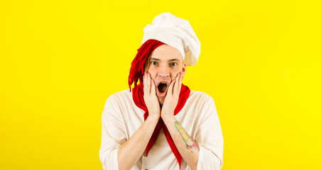 Young chef with shocked facial expression on yellow background. Male cook in white hat and shirt...