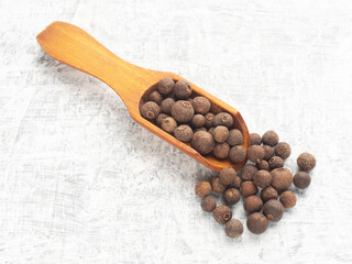 Spice Allspice (Jamaica pepper, Pimento) in wooden scoop and bunch on white concrete background. Macro. Indian cuisine concept
