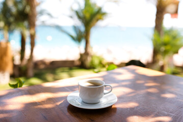 Coffee cup on a wood table over blue sky and sea background. Summer fun, enjoying life, vacations,...