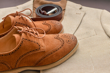 Men brown suede brogue shoes combined with light beige blazer and belt. Selective focus