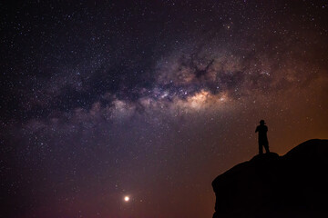 Fototapeta premium Landscape with the Milky Way in the night sky with stars and the shadow of a man standing happily looking at the mountain sky. beautiful universe space background