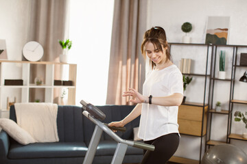 Fototapeta na wymiar Tone your body. Perfect shape. Improving endurance. Portrait of young sportive woman doing cardio at home and looking at the fitness bracelet. Concept of sport, health, action, nutrition