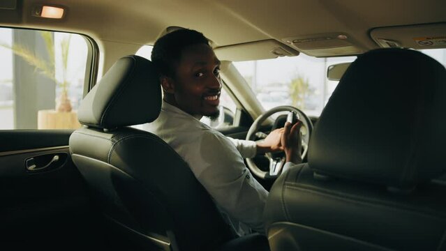 Smiling afro man holding new car keys at vehicle. Handsome man looks satisfied with successful purchase. Eco vehicle. Driver appreciates car purchase in new vehicle at test drive. Starting car engine