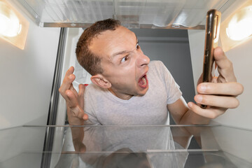 Screaming man is looking for food in refrigerator and is in shock. An empty refrigerator. guy is...