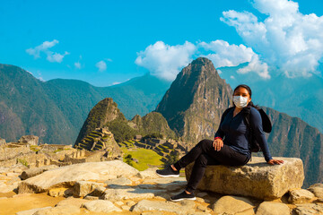 Mujer caucásica con una máscara médica sentada en una roca al fondo de la antigua ciudad de...