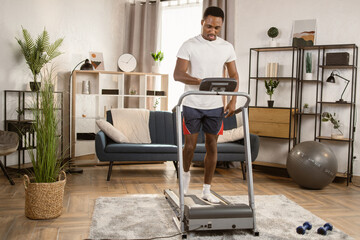 Handsome young sports African man is working out on the background of a bright modern apartment. Doing cardio training on treadmill. Running on treadmill.