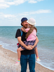 Happy family father daughter hugging on marine landscape. Bearded dad with child in hands having fun together looking on sea water. Authentic lifestyle real people. Travel Fathers day Southern Ukraine