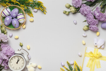 Easter concept on a gray background. Violet flowers and blooming yellow twigs gift eggs in a basket alarm clock.