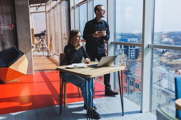 Young business woman behind a laptop wearing glasses sitting at a table having a corporate business meeting with colleagues in a modern office. Business career concept. Free space, selective focus