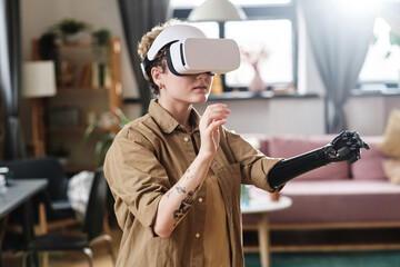 Girl in goggles gesturing with prosthetic arm during her virtual reality game in room