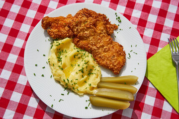Top view picture on the deep fried chicken escalope or schnitzel with mashed potatoes and pickled cucumbers. Served on white plate with green spring napkin and cutlery. Traditional czech cuisine.