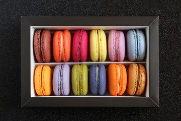 Multicolored macarons in a cardboard box without a lid on a black glitter surface. View from above. Closeup