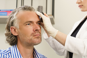 Dermatologist is using dermatoscope for facial skin examination.