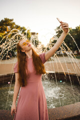 Young beautiful red-haired long-haired woman in a summer pink dress walks through the streets of a summer city.