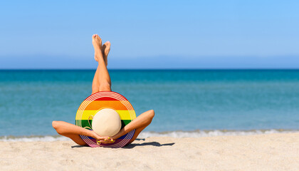 A slender girl on the beach in a straw hat in the colors of the LGBT pride flag. Focus on the hat.
