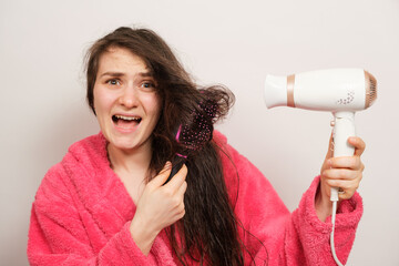 A brunette woman with matted hair dries it with a hair dryer. Hair care, overdried hair