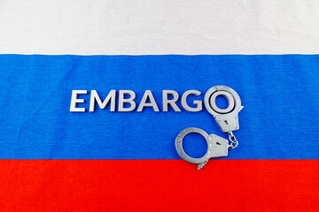 the word embargo laid with silver metal letters on russian tricolor flag with silver handcuffs