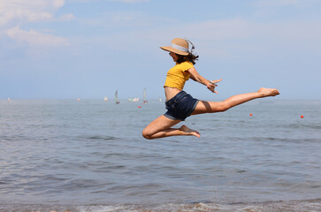 young girl with straw hat performs a very high jump of rhythmic gymnastics
