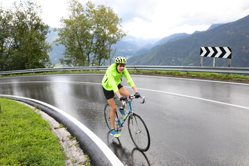 boy cyclist with racing bicycle while making a curve on wet road during sports training while...