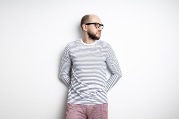 Bearded man with glasses leaned against a white wall