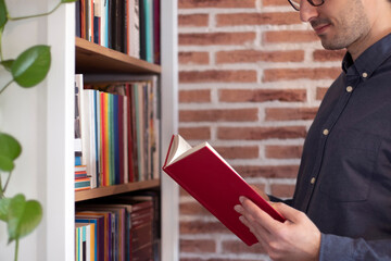 Young smiling man leafing through a book next to a library