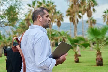 Obraz premium Outdoor portrait of mature man with backpack and laptop in his hands