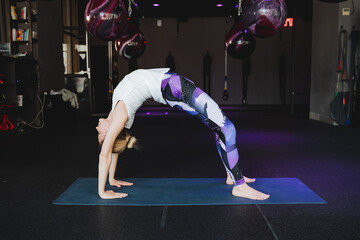 Bridge pose in Yoga Setu Bandha Sarvangasana, an inverted asana girl practices standing on a yoga mat. Asana upside down, back bend back, gym for training.