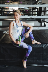 An elegant slender girl sits in the gym, a portrait of a woman fitness trainer with a rope in her hands, a sports model, a thin girl.