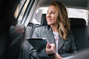 A business woman uses a tablet in the back seat of a car.