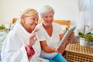 Seniorin im Bademantel winkt in die Webcam am Tablet PC