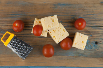 Stack cheese cubes and chery tomatoes with miniature grater on a wood kitchen table