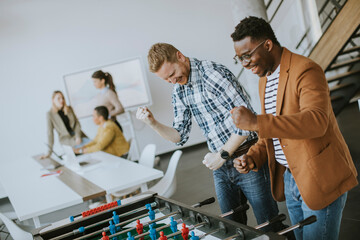 Young casual multiethnic business people playing table football and relaxing at office