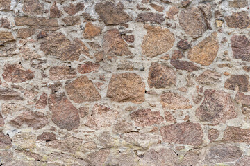 Vintage stone wall background texture. Old natural blocks of granite with different shapes filled with mortar to build a solid masonry. Exterior of an old building. Rough full frame backdrop.