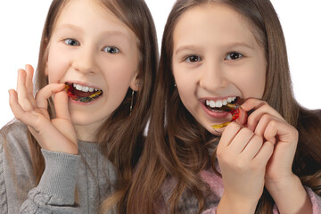 Two cute girls playfully pose with orthodontic appliances in their hands on a white background. The concept of oral hygiene in childhood.