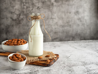 Almond milk in a glass bottle and almonds on a gray marble table. Horizontal photo. Copy space. Top...