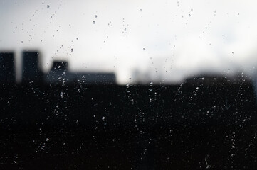 Blurred reflection of city silhouette in glass covered with raindrops