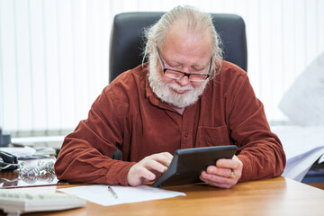 Caucasian man of retirement age counts on a calculator while sitting at table in office room
