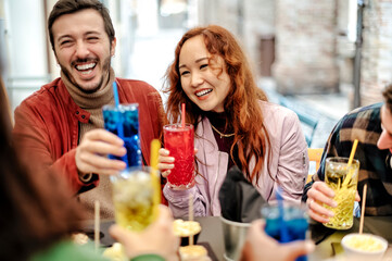 Happy smiling friends drinking and toasting cocktail outside  bar restaurant - Friendship lifestyle concept with young people enjoying time together at open air pub  - Selective focus on Asian girl .