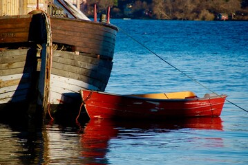 Small red wooden boat beside an old brown worn fishing boat.
